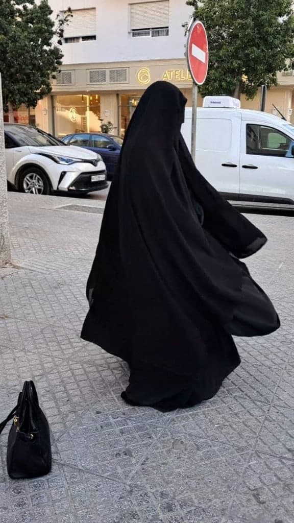 Silhouette noire d'une femme voilée, vue de dos dans la rue, le tissu en mouvement