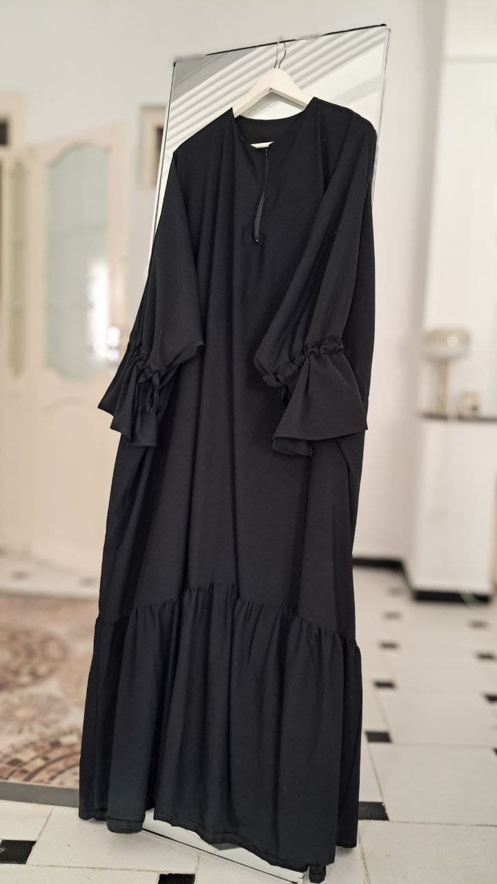 Abaya Sunniya noire de trois quarts devant un miroir, longueur complète